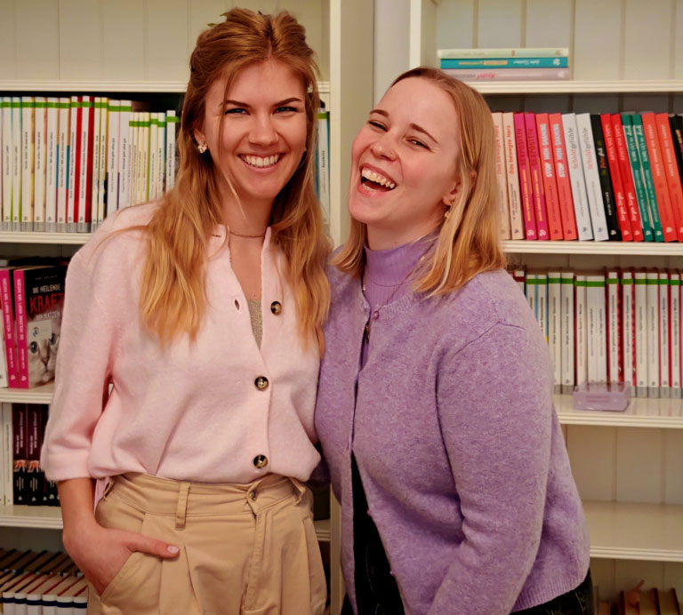Man sieht auf der linken Seite Sarah Bohatschek, die Projektmanagerin von neva und rechts Veronika Holzer, die Interviewführerin. Im Hintergrund ein Buchregal und beide Frauen strahlen.